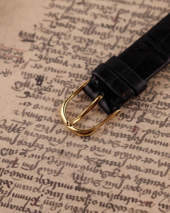 Original Audemars Piguet 18K yellow gold buckle on black leather strap, part of vintage skeleton watch ensemble