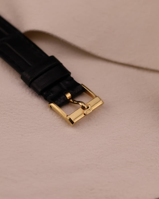 Close-up of original Piaget gold buckle from the top, attached to the black leather strap.