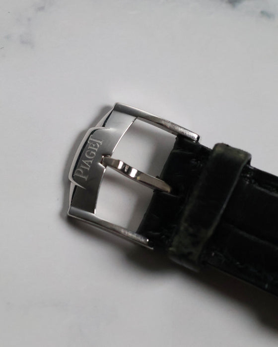 Top view of original Piaget-signed 18K white gold buckle attached to black leather strap.