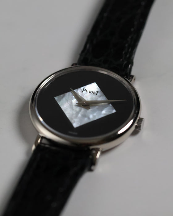 Elegant shot of the Piaget Ref. 922 displayed on a textured surface, showcasing its white gold case, diamond-shaped mother of pearl and onyx dial, and original strap.