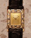 Close-up of a vintage LeCoultre 14K gold Art Deco tank watch showing the gold dial and distinctive raised silver numerals on the outer bezel.