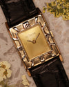 Top-down view of the LeCoultre 14K gold vintage watch with Art Deco numerals bezel, gold dial, and black leather strap on a marble surface.