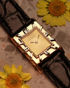 LeCoultre 14K gold tank watch placed on marble with yellow flowers, showcasing the interplay of gold tones and Art Deco numerals bezel.