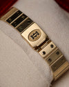 Top-down view of the Cartier Santos Carrée clasp, featuring the engraved Cartier emblem and brushed gold surfaces with polished screws.
