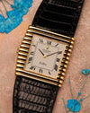 Top-down view of a Rolex Cellini Ref. 4015 in solid 18K yellow gold, showing the asymmetric ribbed case, Roman numeral dial, and black leather strap with blue floral accents.