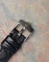 Original Rolex 18K white gold tang buckle with embossed crown logo attached to black leather strap.