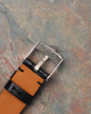 Reverse view of Rolex-signed white gold buckle marked “750,” mounted on black leather strap with tan lining.