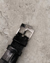 Original Corum steel buckle attached to black leather strap, viewed from above.
