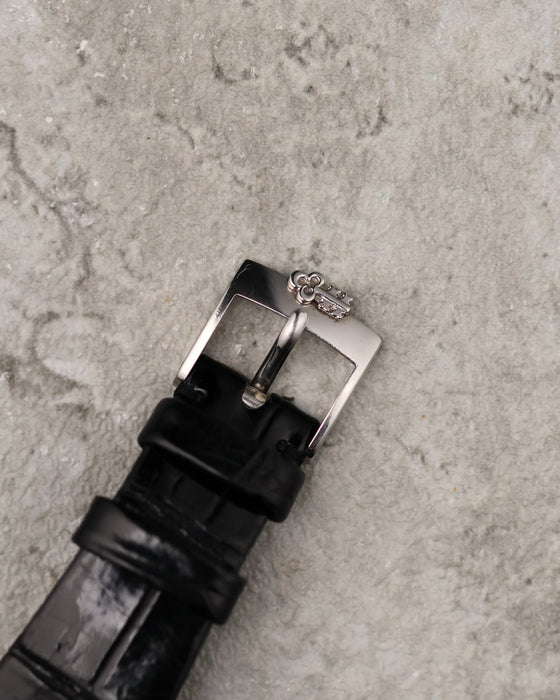 Original Corum steel buckle attached to black leather strap, viewed from above.