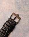 Original 18K white gold Rolex pin buckle attached to black leather strap, viewed from the top.