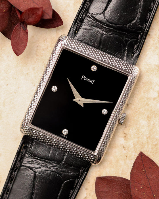 Piaget Ref. 9152 in 18K white gold with woven textured case, black onyx dial and diamond markers, photographed flat lay with black leather strap and red leaves.