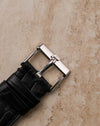 Original 18K white gold Piaget tang buckle attached to black leather strap, top view detail.
