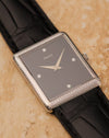 Three-quarter angled view of Piaget 9152 highlighting onyx dial, diamond markers and woven case detailing against light stone background.