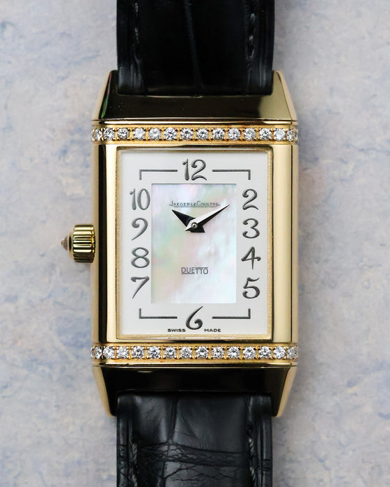 Front dial straight-on showing mother-of-pearl centre and diamond-set top and bottom case edges.