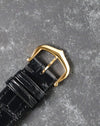 Close-up of original Cartier 18k yellow gold buckle on black leather strap.