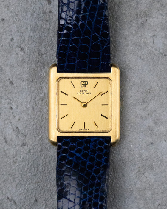 Vintage Girard-Perregaux rectangular watch in 18K yellow gold with gilt dial and blue leather strap.