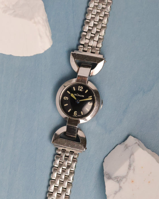 Front view of a 1930s Jaeger-LeCoultre stainless steel back-wind watch with black dial, articulated lugs and vintage plated bracelet.