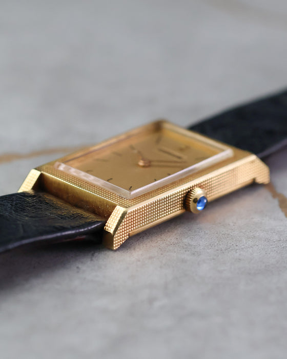 Side profile highlighting the crisp Clous de Paris finishing and blue cabochon crown.