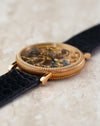 Close side view of the skeletonised movement beneath the crystal and decorative gold case.
