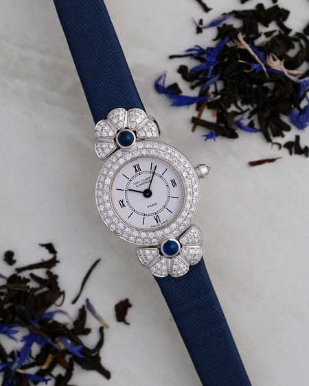Van Cleef & Arpels Ref. 322965 photographed with blue botanicals, showing its diamond-set white-gold case and sapphire cabochons.