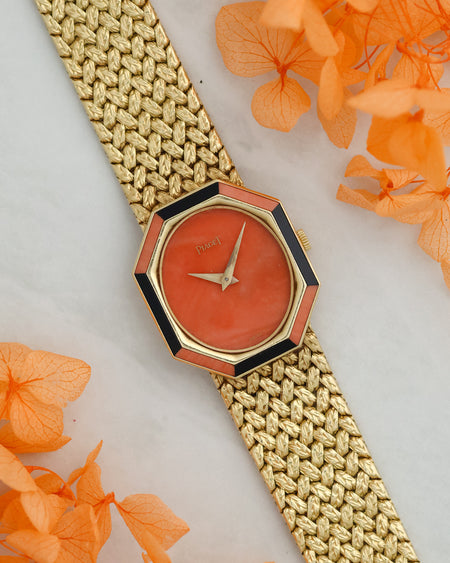 Angled view of the Piaget 9341 D2 showing its coral dial, contrasting onyx bezel inserts and textured yellow-gold bracelet.