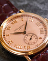 Macro view of the pink guilloché dial with applied Roman numerals, black leaf hands and small seconds.