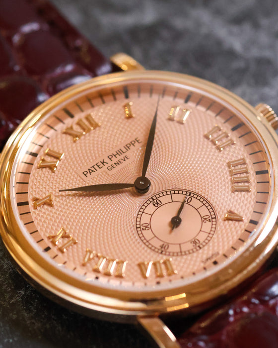 Macro view of the pink guilloché dial with applied Roman numerals, black leaf hands and small seconds.