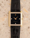 Audemars Piguet rectangular watch with black three-diamond dial and stepped yellow and white gold case on black leather strap.