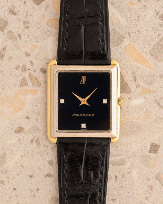 Audemars Piguet rectangular watch with black three-diamond dial and stepped yellow and white gold case on black leather strap.