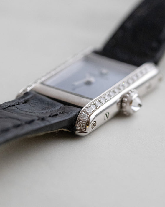 Close-up of the Cartier Mini Tank showing the curved diamond-set case edge and original black leather strap.