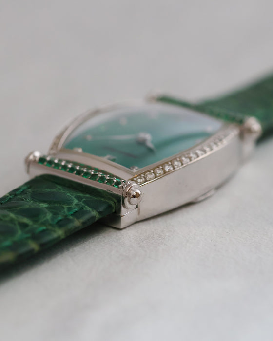 Side profile showing the white gold case thickness, diamond-set bezel and green gemstone-set strap attachment bar.