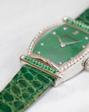 Macro photograph of the green gemstone-set bar, diamond-set bezel and textured green leather strap.