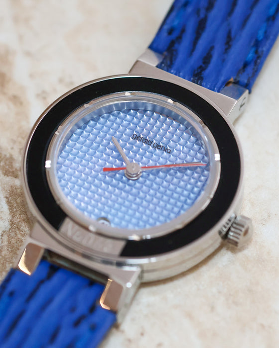 Macro photograph of the light blue geometric dial, silver hands and contrasting red seconds hand.