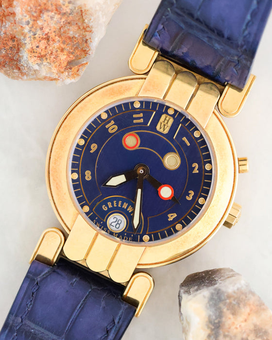 Angled dial photograph of Harry Winston Greenwich GMT showing its blue dial, red-accented GMT hand and date window.