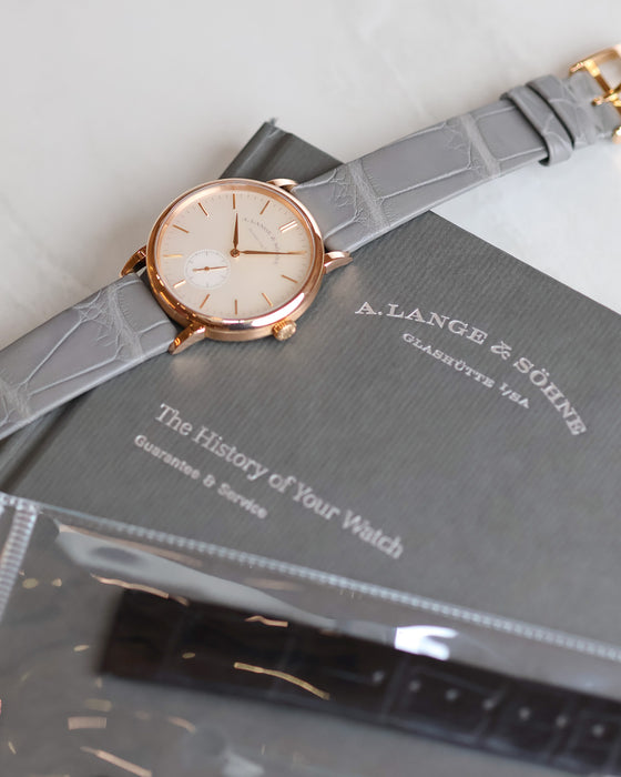 A. Lange & Söhne Saxonia 219.043 in rose gold with a grey alligator strap, photographed on its original presentation booklet.