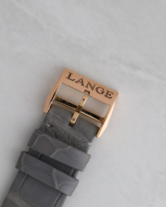 Close-up of the signed Lange rose gold pin buckle and grey alligator leather strap.