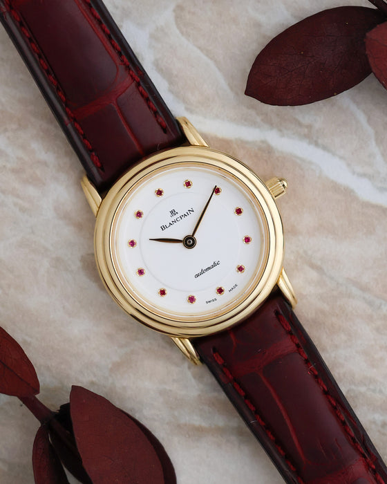 Angled view of the Blancpain Villeret 0096 showing its pink gemstone dial, polished yellow gold case and burgundy leather strap.