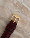 Front view of the Blancpain-signed yellow gold buckle fitted to a burgundy leather watch strap.