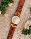 Rolex Orchid ladies' watch photographed diagonally alongside flowers, showing its round case and decorative gold lugs.