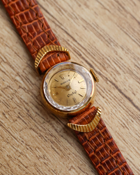 Close-up of the Rolex Orchid champagne dial, applied baton markers, faceted crystal and crescent-shaped gold lugs.