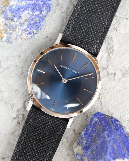 Angled overhead view of an Audemars Piguet blue dial watch photographed alongside blue mineral stones.