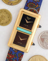 Angled front view of the Chopard Kutchinsky Dual Time beside coins highlighting its onyx dials and turquoise centrepiece.