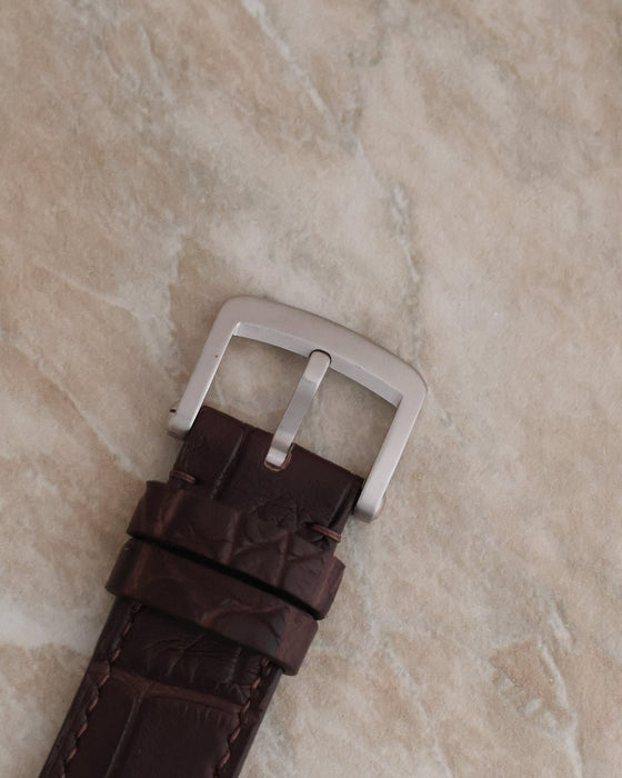 Close-up of the brown leather watch strap and stainless steel pin buckle.