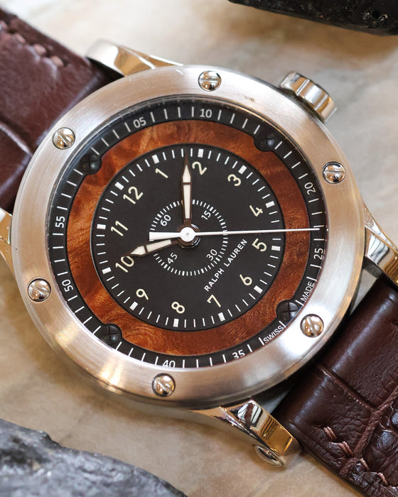 Detailed view of the black dial, natural elm burl wood surround, Arabic numerals and central seconds hand.