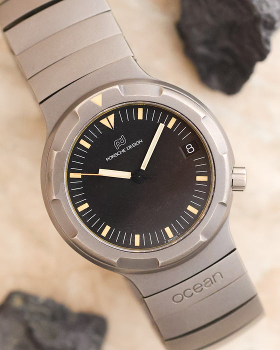 Angled dial photograph of the Porsche Design Ocean 500 featuring its black tritium dial, orange seconds hand and integrated titanium bracelet.
