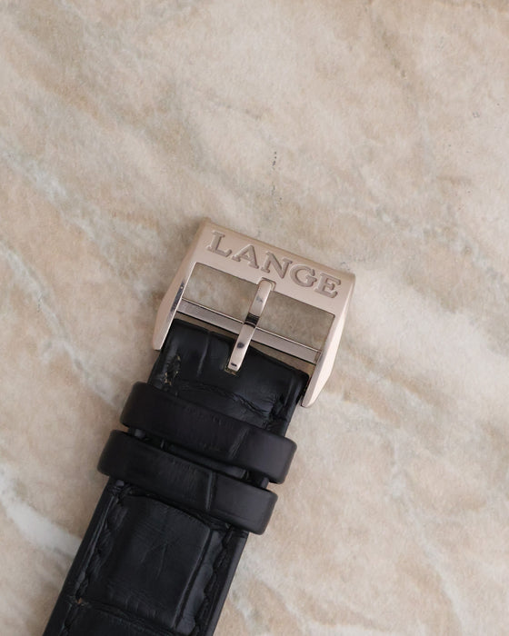 Close-up of the engraved A. Lange & Söhne white gold pin buckle on a black leather strap.