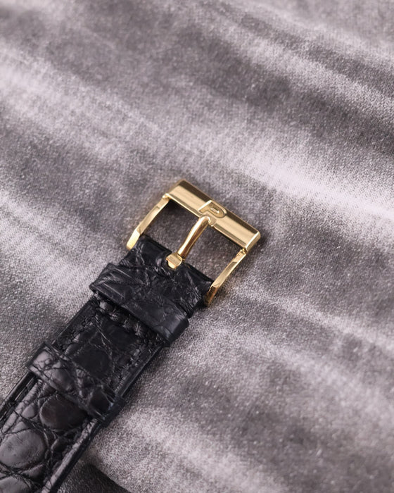 Detail of the original Piaget-signed 18K yellow gold buckle, attached to a black leather strap.